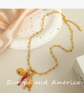 Detail of gold paperclip chain with heart, chili, and rock hand charms on silk background
