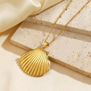 Golden seashell pendant necklace on silk fabric and stone background for beach vacation