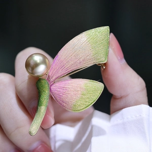Detail einer Emaille Schmetterlingsbrosche mit rosa-grünem Verlauf und goldener Perle