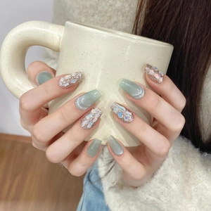 Detail of coffin-shaped press-on nails with green cat-eye finish and seashell shell accents