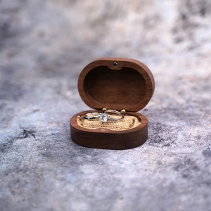 Macro shot of oval dark wood ring box with silver diamond rings on linen lining