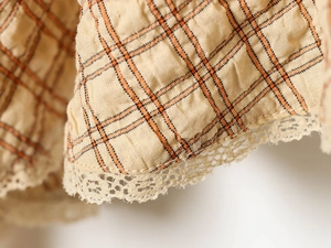 Close-up of beige plaid fabric with orange lines and delicate white lace trim detail