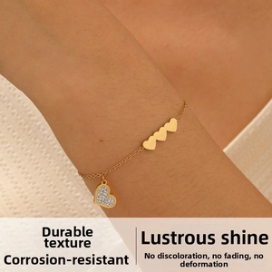 Detailed close-up of a gold heart charm bracelet with sparkling zircon on a wrist