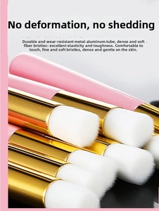 Close-up of soft white fiber bristles and gold aluminum ferrule on a pink cleaning brush