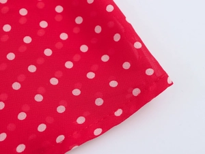Dettaglio ravvicinato del tessuto rosso a pois per un abito lungo con scollo a V e fiocco