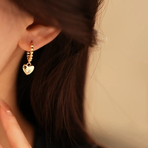 Dettaglio di un orecchino a cuore d'oro con un piccolo diamante indossato da una modella