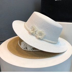Close-up of straw boater hats with pearl bands and floral details on white podium