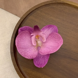 Detail of vibrant magenta faux orchid hair clip with realistic spots on dark wooden tray