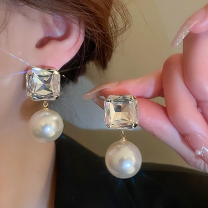 Detail of square crystal earrings with round pearl drop on female model ear