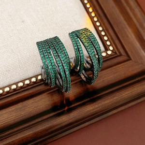 Close-up of multi-layer C-shaped dark metal earrings with green cubic zirconia stones