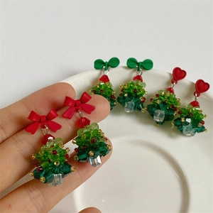 Detail of handmade beaded Christmas tree earrings with red bows on a ceramic tray