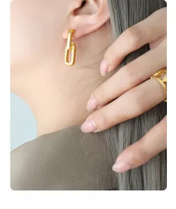 Close-up of interlocking U-link earrings and hollow geometric ring in matte gold finish