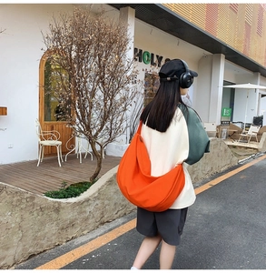 Action shot of a large bright orange oxford hobo bag with a wide crossbody shoulder strap