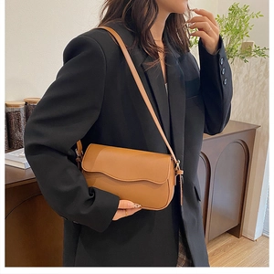 Brown leather crossbody bag shown on model's shoulder with black suit for size reference