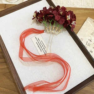 Detail view of deep red fabric flowers on golden hairpin with sheer orange ribbon