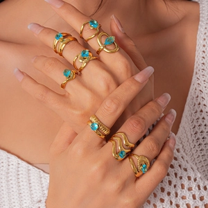 Vue détaillée de bagues en acier doré empilables avec zircon bleu sur la main d'un mannequin