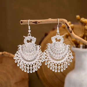 Ethnic peacock hollow tassel earrings with silver filigree finish on wooden stand