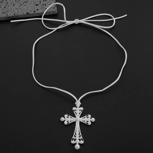Détail du pendentif croix évidée en argent avec perles et nœud en ruban blanc sur noir