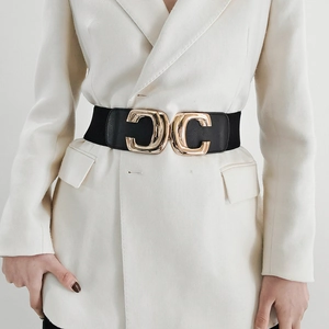 Women's elastic waist belt with large gold interlocking buckle on white blazer
