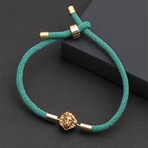 Detail of teal braided bracelet with golden lion head charm on leather background