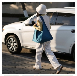 Blue nylon tote bag styled as a shoulder bag on a model in an urban outdoor setting