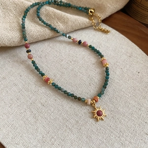 Collier de perles ethniques avec perles cyan foncé et pendentif soleil doré sur lin