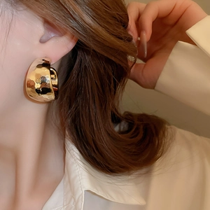 Close-up of golden C-shaped hoop earring with textured rhombus pattern on model