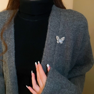 Detail of silver butterfly brooch with teardrop zircons pinned on a grey knit cardigan