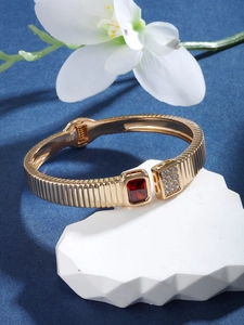 Detail of gold open bracelet with red gemstone and cubic zirconia on white stone