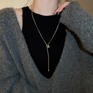 Detail of a gold plated Y-shaped necklace with a square zircon pendant on a model