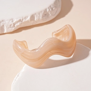 Macro detail of wave-shaped beige acrylic cuff bracelet with marble texture