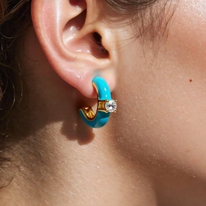 Detail of C-shaped golden earring with blue enamel and sparkling zircon on ear