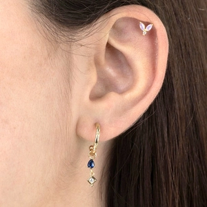 Gold waterdrop earrings with blue gemstones and purple leaf cartilage stud on model