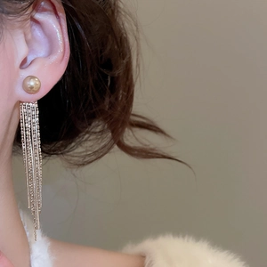 Detail of golden tassel pearl stud earrings worn by model with elegant tassel texture
