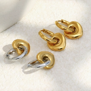 Détail de boucles d'oreilles cœur pendantes en finition or et argent sur fond de pierre