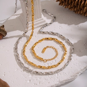 Close-up of gold and silver geometric link chains on white stone and pinecone