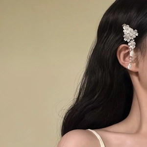 Side view of a delicate white flower tassel hair clip with pearls on black wavy hair