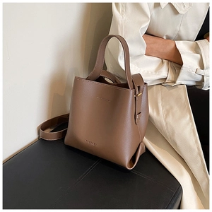 Brown leather bucket bag detail with shoulder strap and brand logo in urban setting