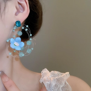 Detail view of a blue fabric flower earring with beads on a model side profile