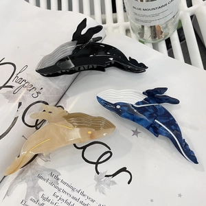 Three whale-shaped acetate hair claws in marble and black colors on a lifestyle background