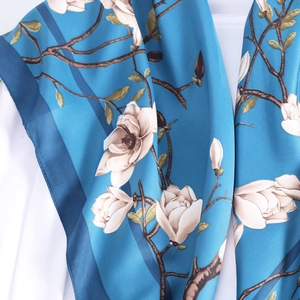 Detail of silk-textured blue scarf showing white magnolia print and fabric draping