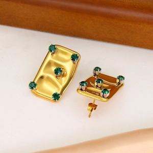 Detailed macro view of gold plated earrings featuring green zircons on a wavy metal base