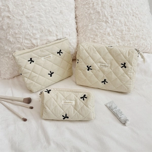 Three-piece beige quilted cosmetic bags set with black embroidered bows for travel