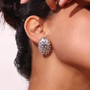 Detail of silver oval stud earrings with 3D spike texture worn on a model's ear