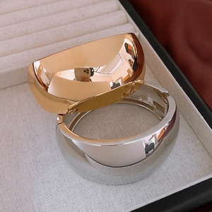 Polished minimalist wide cuff bracelets in gold and silver finish on a soft velvet tray
