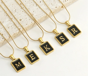Detail of 18k gold plated snake chains with black rectangular initial letter pendants