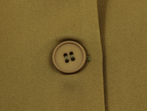 Close-up of a brown four-hole button on camel-colored woven fabric with twill texture