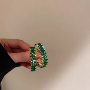 Macro detail of large gold hoop earrings set with marquise-cut emerald green gemstones