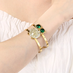 Detail view of golden owl cuff bracelet with green gemstones and white enamel on wrist