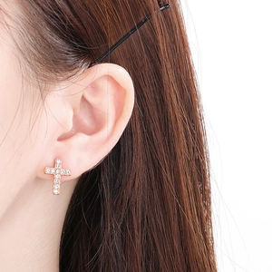 Close-up of sparkling cross earrings with small rhinestones on female ear lobe